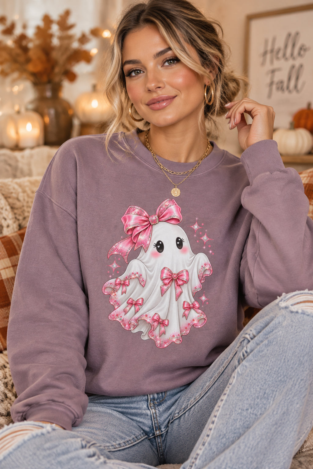 A dusty purple crewneck sweatshirt featuring a cute cartoon ghost graphic on the front. The ghost is white with pink bows, black eyes, and pink sparkles, set against a clean white background.