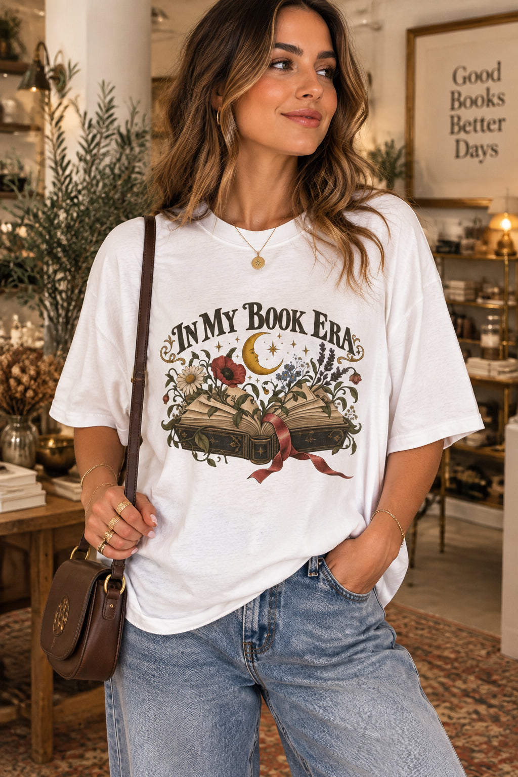 A white short-sleeve crewneck t-shirt featuring a vintage-style graphic on the front with the text 'IN MY BOOK ERA' above an illustration of an open book, stars, and flowers.