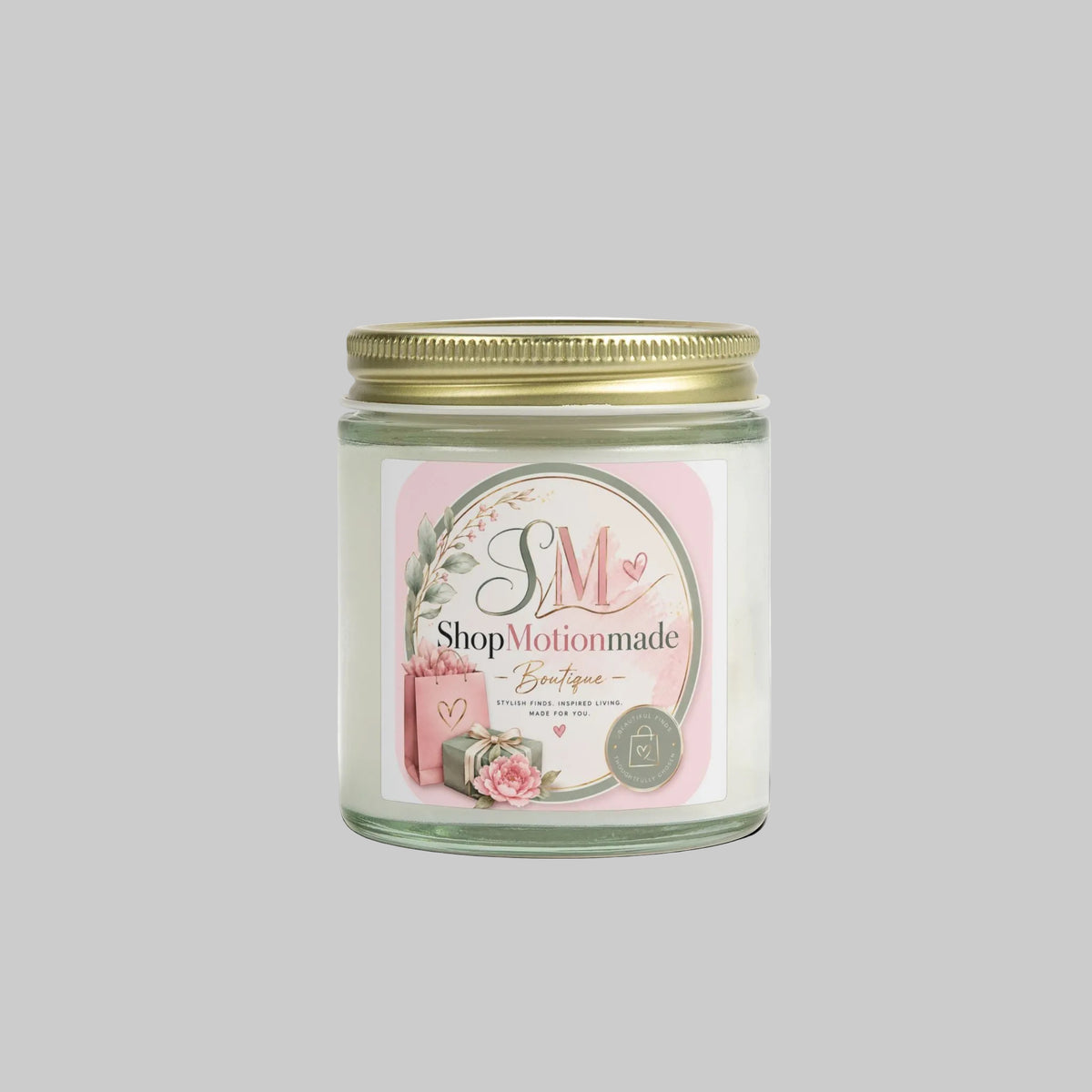 A glass jar candle with a gold metal lid and a white label featuring a pink circle, floral illustration, and the ShopMotionmade Boutique logo, shown on a white background with a soft shadow.